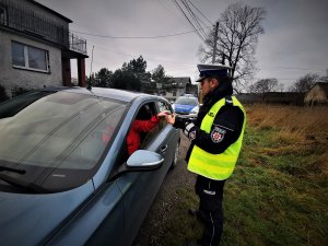 policjant drogówki rozmawia z zatrzymanym do kontroli kierującym samochodem osobowym koloru jasnoniebieskiego