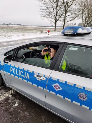 policyjny radiowóz, w środku, za kierownicą siedzi policjant drogówki, patrzy przez lornetkę