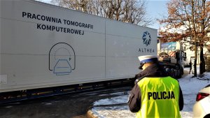 policjant drogówki w odblaskowej kamizelce, w tle transport pracowni tomografii