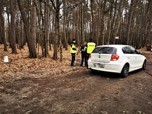 dwóch policjantów i mężczyzna stoją obok białego samochodu, w tle las