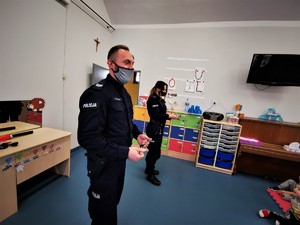 policjanci (kobieta i mężczyzna) w trakcie zajęć profilaktycznych z przedszkolakami. Scena ma miejsce w jednej z sal.