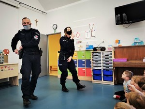 policjanci (kobieta i mężczyzna) w trakcie zajęć profilaktycznych z przedszkolakami. Scena ma miejsce w jednej z sal.