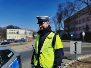 policjant drogówki stoi przy radiowozie i uśmiecha się. Piekna, słoneczna pogoda