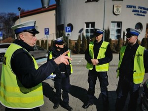 naczelnik drogówki rozmawia ze swoimi policjantami. Wszyscy mają założone odblaskowe kamizelki