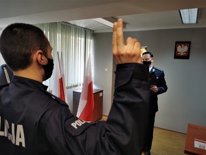 młody policjant z podniesioną prawą ręką składa rotę ślubowania, przed nim komendant