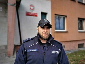 umundurowany policjant stoi przed budynkiem komendy