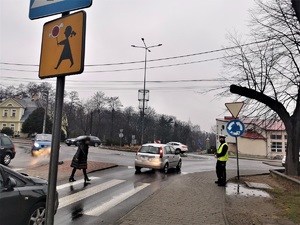 policjant drogówki przygląda się pieszym i kierującym pojazdami w centrum miasta w rejonie oznakowanego przejścia dla pieszych