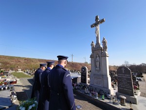 trzech policjantów stoi przed pomnikiem, scena ma miejsce na cmentarzu