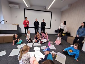 sala konferencyjna w budynku biblioteki, uczestnicy spotkania, dzieci i ich opiekunowie, w tyle dyrektor oraz policjanci