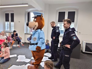 sala konferencyjna w bibliotece, dwóch dzielnicowych, policyjna maskotka, siedzący na krzesłach ludzie