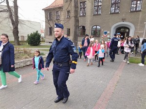 dzielnicowy przed budynkiem biblioteki, za nim dzieci i ich opiekunowie