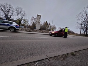 policyjny radiowóz, policjant na drodze, samochód osobowy, w tle pomnik