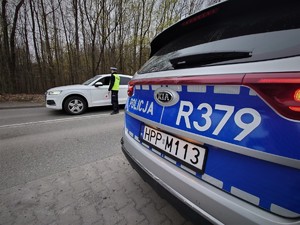 na pierwsyzm planie policyjny radiowóz, w tle samochód osobowy i policjant