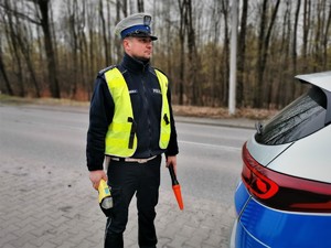 policjant drogówki stoi obok radiowozu, trzyma w ręce latarkę oraz urządzenie do badania stanu trzeźwości