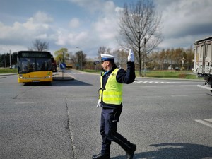 policjant drogówki stoi na środku skrzyżowania i kieruje ruchem. W tle autobus miejski