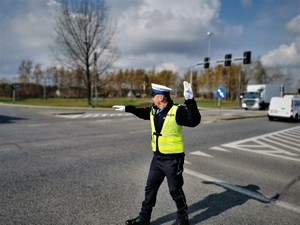 policjant drogówki stoi na środku skrzyżowania i kieruje ruchem. W tle samochody