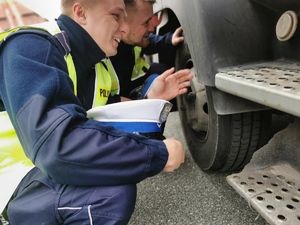 policjanci drogówki kontrolują samochód ciężarowy, kucają i sprawdzają podwozie