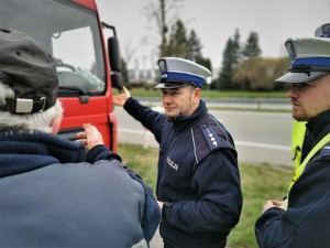 wykładowca Szkoły Policji wskazuje ręką na ciężarówkę. Obok niego policjanci kursu oraz kierowca pojazdu