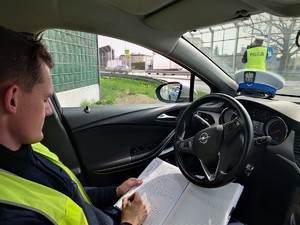 siedzący w radiowozie policjant, który dokumentuje przebieg służby