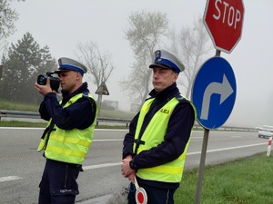 policjanci drogówki stoją przy trasie i dokonują pomiaru prędkości