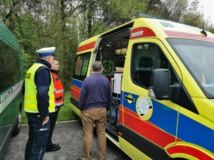 karetka pogotowia, obok niej policjant, mężczyzna wchodzi do karetki