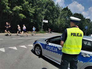policjant stoi obok radiowozu, w tle biegacze