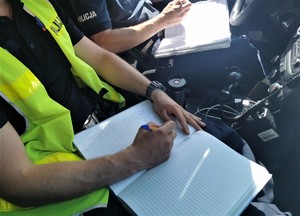 policjant siedzi w radiowozie i wpisuje coś do notatnika