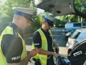policjanci drogówki w odblaskowych kamizelkach pakują sprzęt do radiowozu