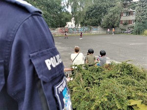 fragment policyjnego munduru, w tle dzieci jeżdżące na rolkach