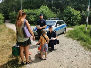 policjanci rozmawiają z dziećmi oraz ich opiekunką, za nimi stoi radiowóż