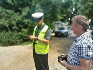 policjant drogówki sprawdza dokumenty kierowcy, w tle radiowóz