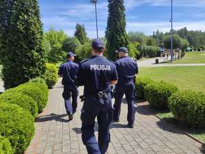 trzech policjantów idących chodnikiem, w tle obiekt rekreacyjny w Łaziskach Górnych
