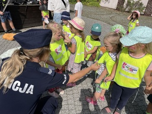 policjantka rozmawia z przedszkolakami, dzieci mają ubrane odblaskowe kamizelki