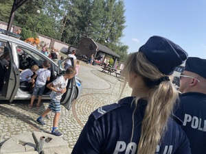 policjanci patrzą na biegające po podwórku dzieci, widać radiowóz