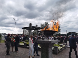 zdjęcie płonącego znicza. W tle uczestnicy uroczystości