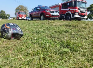 leżący na trawie kask motocyklisty, w tle wozy służb