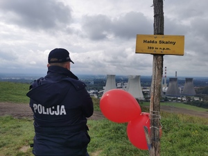 zdjęcie kolorowe: policjant w umundurowaniu, z tyłu napis POLICJA, mężczyzna patrzy na panoramę miasta, obok tabliczka: HAŁDA SKALNY, 389 metra nad poziomem morza