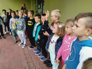 grupa uczniów klas pierwszych stoi przed budynkiem szkoły. Dzieci stoją w szeregu