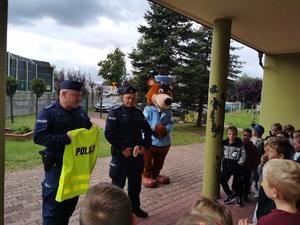 Jeden z policjantów prezentuje dzieciom kamizelkę odblaskową z napisem POLICJA