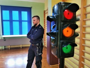 zdjęcie kolorowe: atrapa sygnalizatora świetlnego, w tle policjant w mundurze