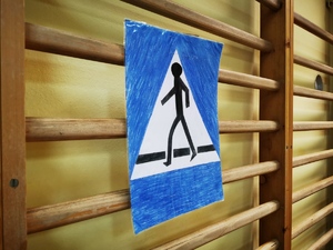 namalowany na kartonie znak drogowy: przejście dla pieszych, przyczepiony do barierek sali gimnastycznej