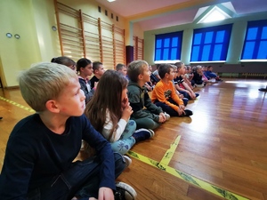 siedzące na sali gimnastycznej dzieci klas pierwszych podczas zajęć profilaktycznych
