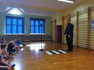 zdjęcie kolorowe: sala gimnastyczna szkoły, dzielnicowi rozmawia z siedzącymi na podłodze dziećmi