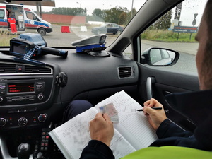 policjant drogówki siedzi w środku radiowozu i dokonuje wpisu w notatniku służbowym