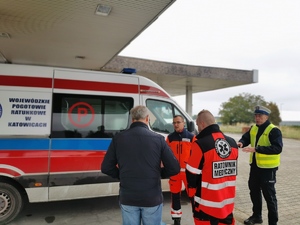 na zdjęciu widać karetkę pogotowia, obok niej stoją dwaj ratownicy medyczni, policjant oraz kierujący, który został zatrzymany do kontroli