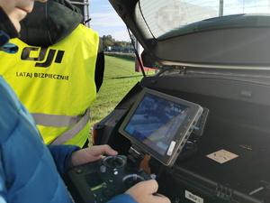 policjant steruje dronem, obok niego drugi policjant w kamizelce z napisem &quot;DJI Lataj Bezpiecznie&quot;