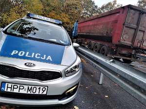 policyjny radiowóz, obok niego samochód ciężarowy. Oba pojazdy stoją na parkingu przy ulicy Gliwickiej, tuż przy lesie