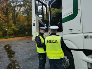 dwóch policjantów drogówki rozmawia z kierowcą ciężarówki. Mundurowi mają założone odblaskowe kamizelki