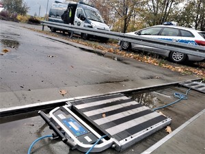 rozłożone na parkingu urządzenie do kontroli nacisku samochodu ciężarowego na jezdnię, w tle policyjny radiowóz