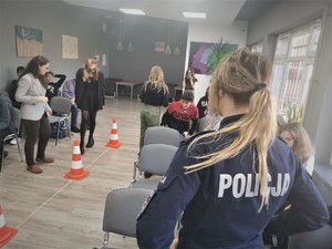 młodzież szkolna podczas zajęć praktycznych. Scena ma miejsce w budynku szkoły. Na środku sali rozstawione pachołki. Widać też policjantkę oraz pracownicę Sanepidu